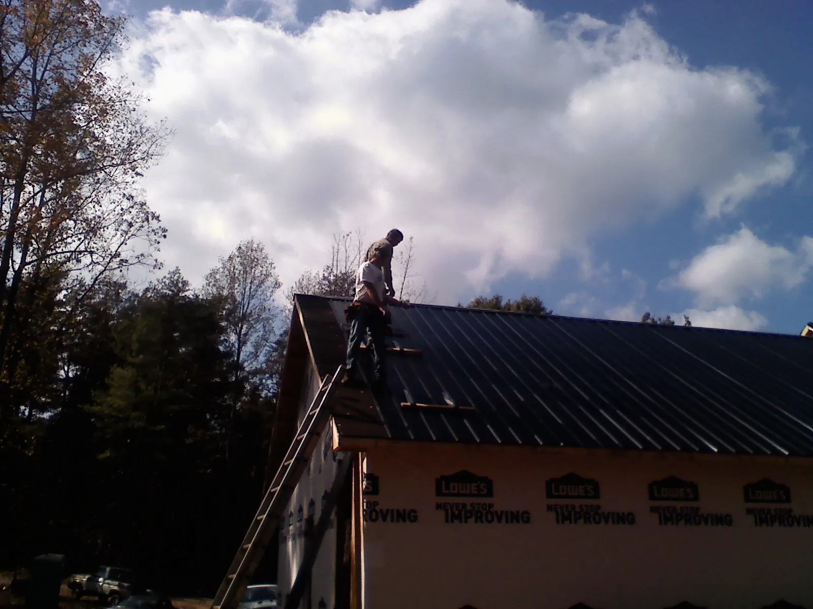 Roofer fastening dark metal panels high against a cloudy sky, from a Roof Inspection job in Lincoln